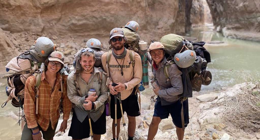 a group of gap year students wearing backpacks stand in a canyon with water in the background